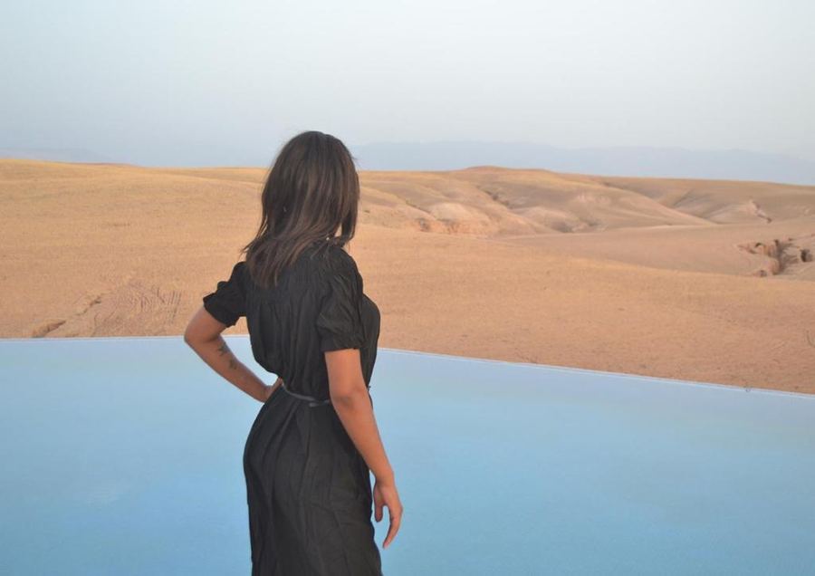 Woman at infinity pool edge overlooking vast Agafay Desert landscape — Marrakech desert camp
