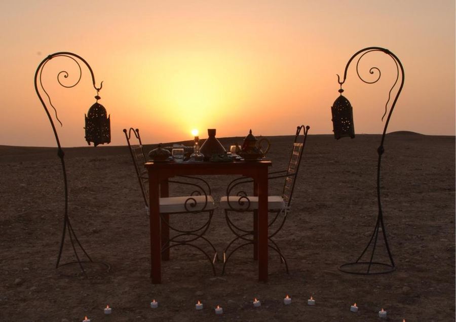 Romantic private dinner table with Moroccan lanterns in open desert at golden sunset — Agafay near Marrakech