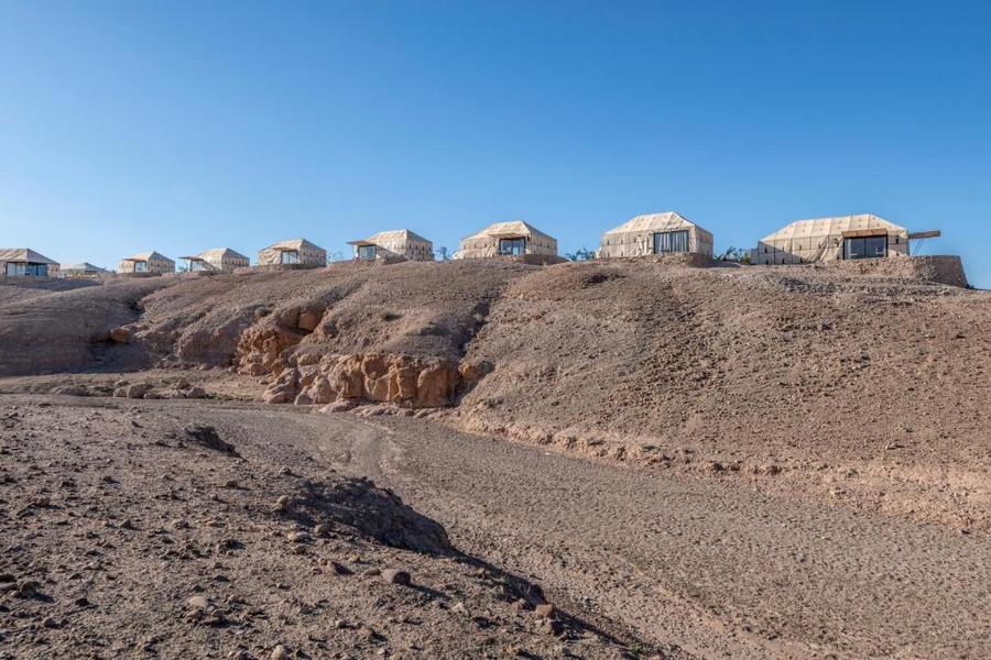 Row of luxury canvas tents on rocky Agafay Desert ridge under clear blue sky — glamping near Marrakech
