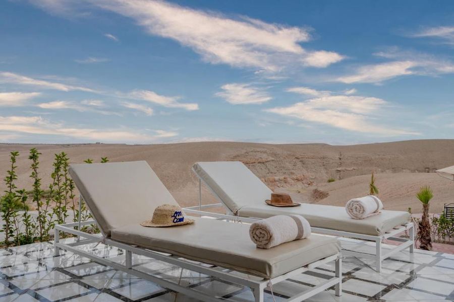 Two white sun loungers with hats and towels facing Agafay Desert — luxury camp terrace