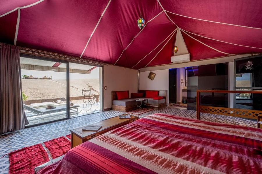 Luxury red ceiling tent suite with private terrace and Agafay Desert view through glass doors