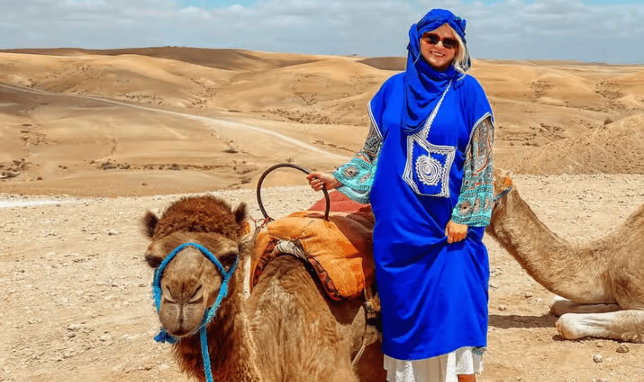 Mujer con vestimenta bereber azul de pie junto a un camello