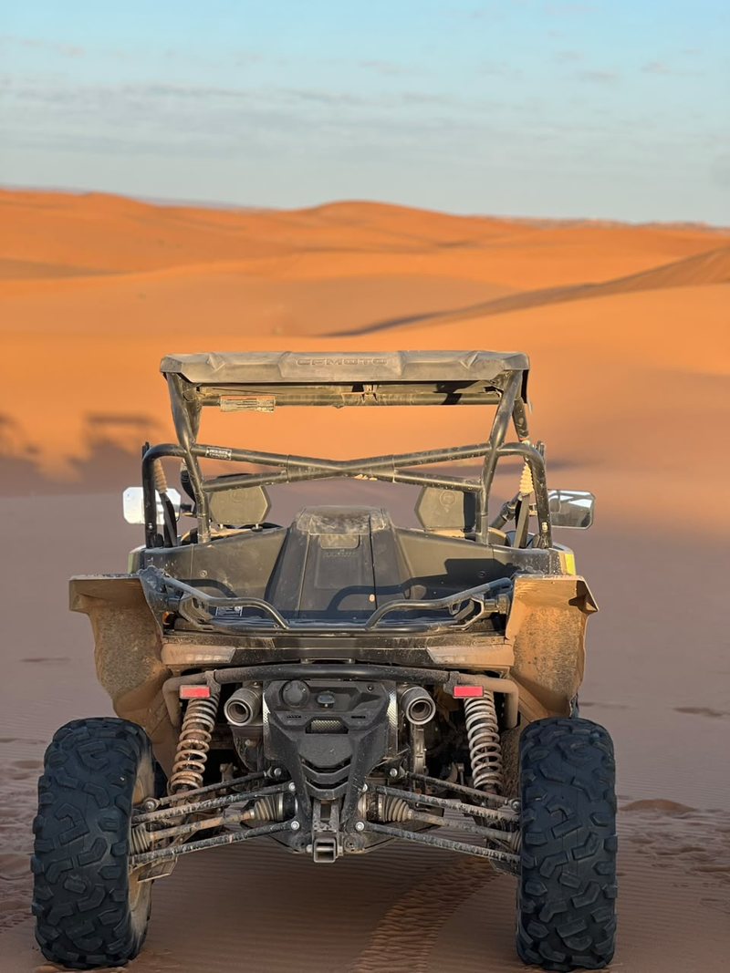 Vista trasera de un buggy CFMoto detenido sobre la arena naranja de las dunas