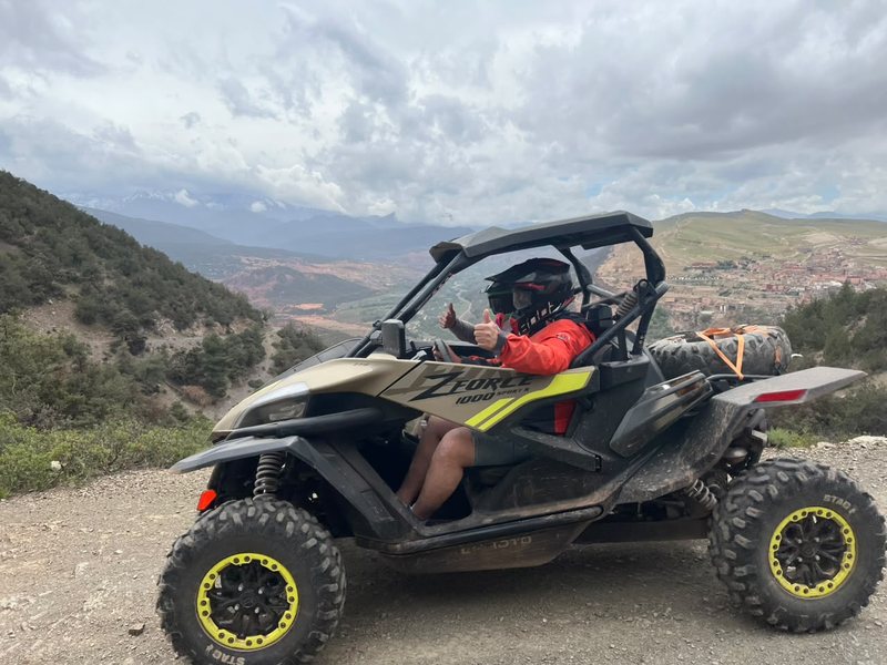 Piloto con el pulgar en alto al volante de un buggy CFMoto ZForce en una carretera de montaña sobre un valle