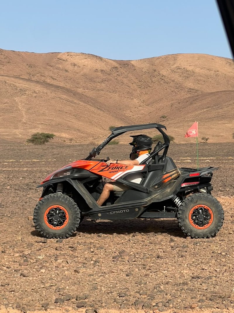 Buggy naranja CFMoto ZForce con una bandera de seguridad roja en un desierto de piedras