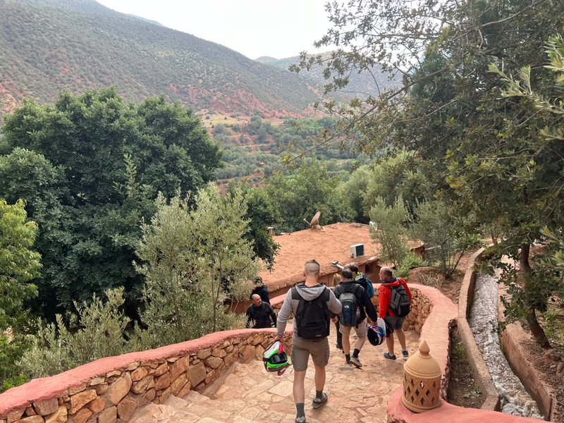 Pilotos con el casco en la mano bajando una escalera de piedra en un valle verde
