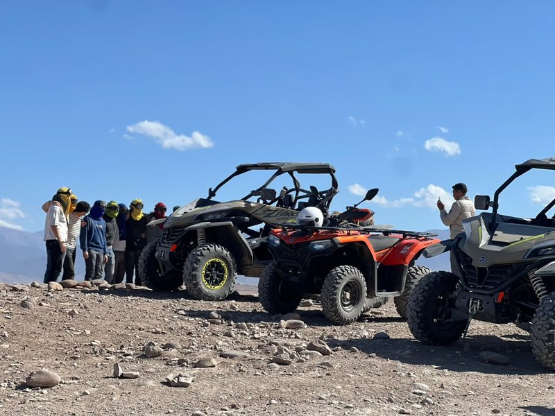 Grupo de pilotos con pañuelos de colores junto a buggys y un quad mientras un guía hace una foto
